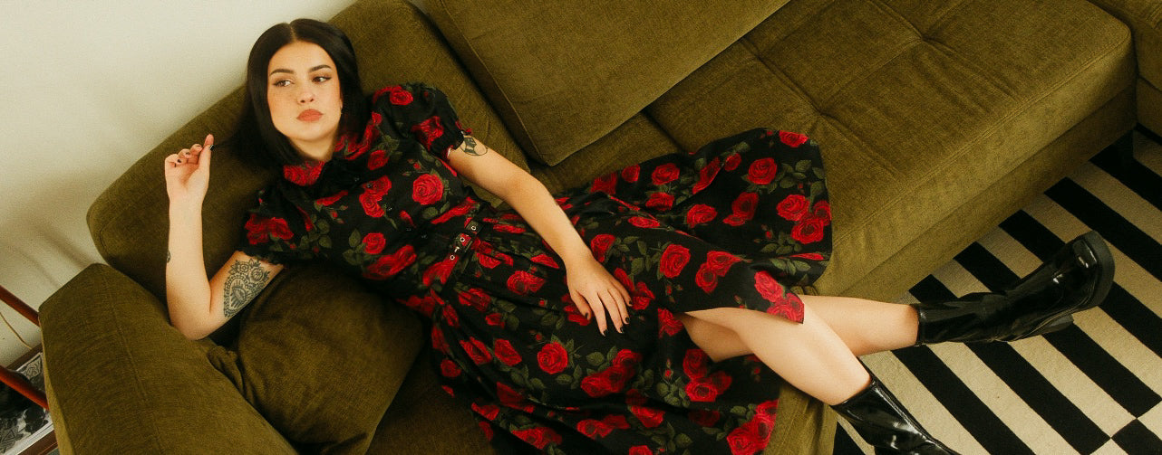 Woman in a black and red floral dress lying on a green couch with a striped floor.